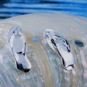 May include: Two silver flip-flop charms on a white iridescent shell background.