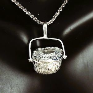 Könnte beinhalten: Eine silberne Halskette mit einem kleinen, detaillierten, klappbaren Korb-Anhänger. Der Korb hat eine geflochtene Textur und einen Griff.