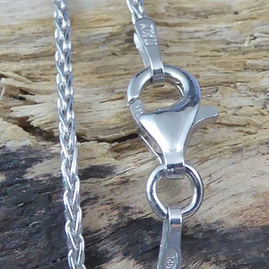 May include: A silver chain necklace with a lobster clasp. The chain is a braided design and the clasp is marked with "925".