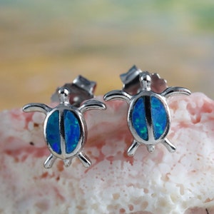 Könnte beinhalten: Ein Paar silberne Schildkröten-Ohrstecker mit blauen Opal-Einlagen. Die Ohrringe sind klein und zart, perfekt für den täglichen Gebrauch.