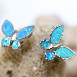 May include: A pair of silver butterfly earrings with blue opal accents. The earrings are small and delicate, perfect for everyday wear.