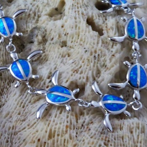 May include: A silver chain bracelet with blue opal turtle charms. The turtles are facing different directions and are connected by a silver chain.
