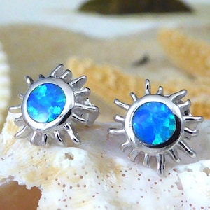 Könnte beinhalten: Ein Paar silberne Ohrstecker mit einem blauen Opal-Stein, der in einem Sonnenstrahl-Design gefasst ist.