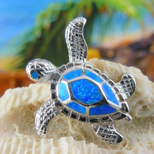Könnte beinhalten: Ein silberner Schildkrötenanhänger mit einer blauen Opal-Schale. Die Schildkröte ist detailliert mit einer strukturierten Schale und einer glatten, polierten Oberfläche.