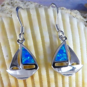 Puede incluir: Un par de pendientes de plata en forma de velero con detalles de ópalo azul. Los pendientes tienen un diseño sencillo y son perfectos para el uso diario.
