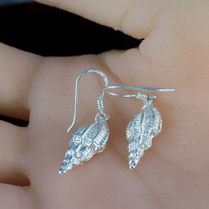 May include: A pair of silver dangle earrings featuring a detailed seashell design. The earrings have a hook closure.