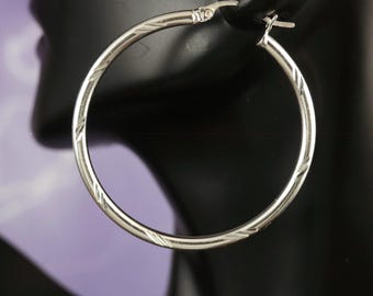 May include: Silver hoop earrings with a textured design. The earrings are on a black display stand.