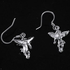 K&ouml;nnte beinhalten: Ein Paar silberne Ohrh&auml;nger mit einem detaillierten Engelsmotiv. Die Engel haben Fl&uuml;gel und befinden sich in einer fliegenden Pose.