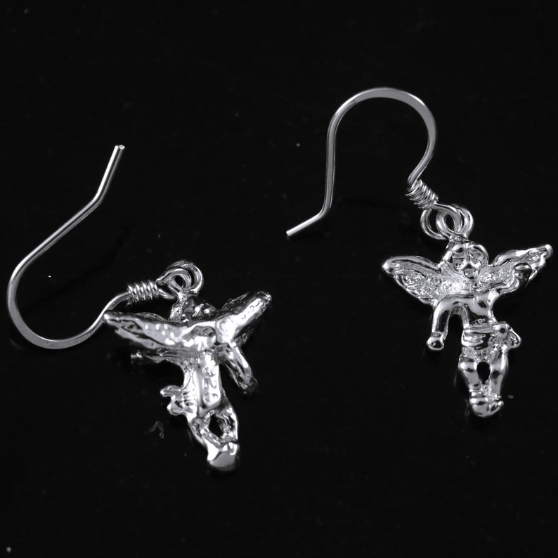 K&ouml;nnte beinhalten: Ein Paar silberne Ohrh&auml;nger mit einem detaillierten Engelsmotiv. Die Engel haben Fl&uuml;gel und befinden sich in einer fliegenden Pose.