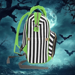 Puede incluir: Una mochila de rayas blancas y negras con detalles verdes. La mochila tiene cierre de cremallera y un peque&ntilde;o bolsillo en la parte delantera.
