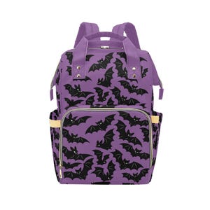 Peut inclure: Un sac à dos violet avec un motif répétitif de chauves-souris noires aux yeux blancs. Le sac comprend une poignée supérieure, deux bretelles, un compartiment principal zippé et une poche avant zippée plus petite avec des détails latéraux clairs.