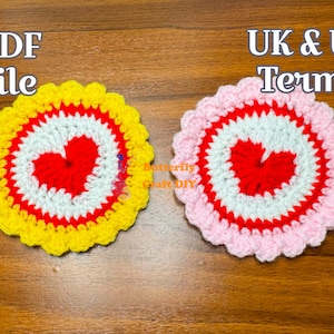 Peut inclure: Deux dessous-de-verre en crochet avec un motif de cœur au centre. Le dessous-de-verre de gauche est jaune, rouge et blanc. Le dessous-de-verre de droite est rose, rouge et blanc. Le texte "PDF file" est au-dessus du dessous-de-verre de gauche et le texte "UK & US Terms" est au-dessus du dessous-de-verre de droite.