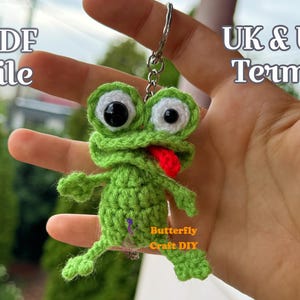May include: A handmade green crochet frog keychain with a red tongue and large white and black eyes. The frog is attached to a silver keyring. The image also includes the text "PDF file" and "UK & US Terms".