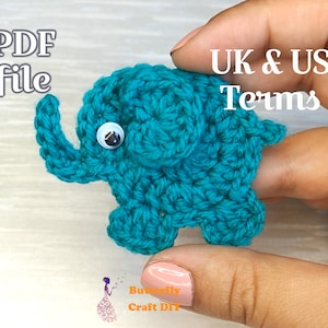 Puede incluir: Un juguete de amigurumi de elefante de crochet de color turquesa con ojos blancos. El juguete está siendo sostenido por una mano. El texto "UK & US Terms" es visible en la imagen.