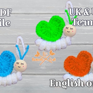 May include: Three handmade crochet snail ornaments with heart-shaped shells in blue, green, and orange. Each snail has a white body, wooden head with a painted face, and yarn antennae. The image includes the text "PDF file" and "English only".