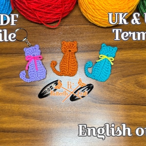 May include: Crocheted cat keychains in purple, orange, and turquoise, each with a ribbon bow. The image includes text that reads "PDF file", "UK & US Terms", and "English only". The keychains are displayed on a wooden surface.