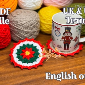 May include: A handmade crochet coaster with a red, white, and green floral design sits on a wooden surface. A mug with a nutcracker design rests on a matching coaster. The image includes balls of yarn and text that reads "PDF file" and "English only".