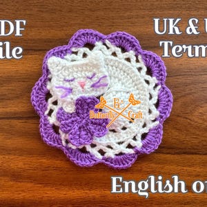 May include: A round crochet coaster featuring a white sleeping cat with purple whiskers and a pink nose, resting on a white circular base with a purple scalloped border. A purple flower is attached to the cat. Text reads: PDF file, UK & US Terms, Butterfly Craft, English only.