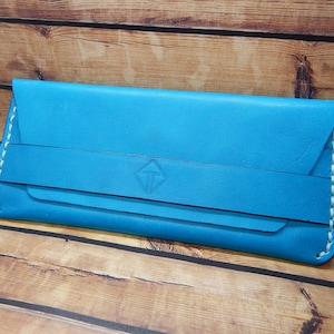 Puede incluir: Una cartera de cuero azul claro con costuras blancas y un logotipo en forma de diamante.