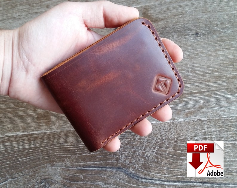 May include: A brown leather wallet with a stitched border and a geometric logo. The wallet is held in a hand, showcasing its rich color and texture. The wallet appears to be approximately 4 inches wide and 3 inches tall.