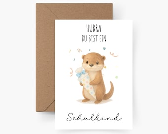 May include: A white card with a brown envelope. The card has a cartoon otter holding a colorful cone with a blue bow. The text on the card reads "Hurra Du Bist Ein Schulkind".