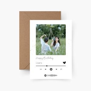 Könnte beinhalten: Eine weiße Geburtstagskarte mit einem Foto von zwei Personen auf einem Feld, dem Text "Happy Birthday Laura" und einem Musikplayer-Design. Die Karte wird von einem braunen Umschlag begleitet.