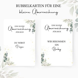 Op de afbeelding: Twee witte kaarten met groen gebladerte en gouden glitter. De tekst op de kaarten luidt "Eine kleine &Uuml;berraschung" en "F&Uuml;R DICH". E&eacute;n kaart zegt "DU WIRST Papa" en de andere zegt "WIR BEKOMMEN EIN Baby".