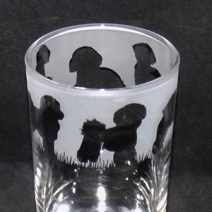 May include: A frosted glass tumbler featuring a silhouette design of several dogs. The dogs are in various poses, including sitting, standing, and playing. The glass is clear and has a smooth, rounded base.