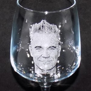 May include: A clear glass wine glass with a man's face etched into the side.