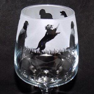 May include: A clear glass wine glass with etched silhouettes of dogs. The dogs are in various poses, including running and standing. The glass is frosted and has a stem.
