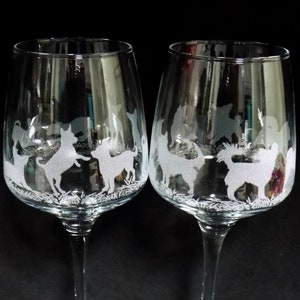 May include: Two clear wine glasses with etched dog silhouettes. One glass is labelled "Short haired" and the other "Long haired". The dogs are depicted in various playful poses, with grass detail at the base of the design. The glasses have a classic stem and base.