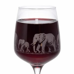 May include: A clear wine glass filled with red liquid. The glass has an etched design of a family of elephants. The stem is long and slender, and the base is round. The glass is filled with red liquid.
