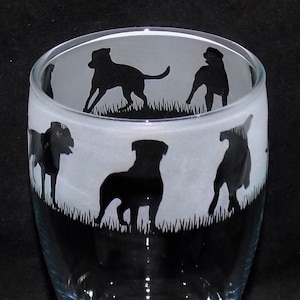May include: A clear glass tumbler with a frosted design of five black silhouettes of dogs. The dogs are in various poses, including standing, sitting, and running. The glass has a rounded bottom and a wide mouth.