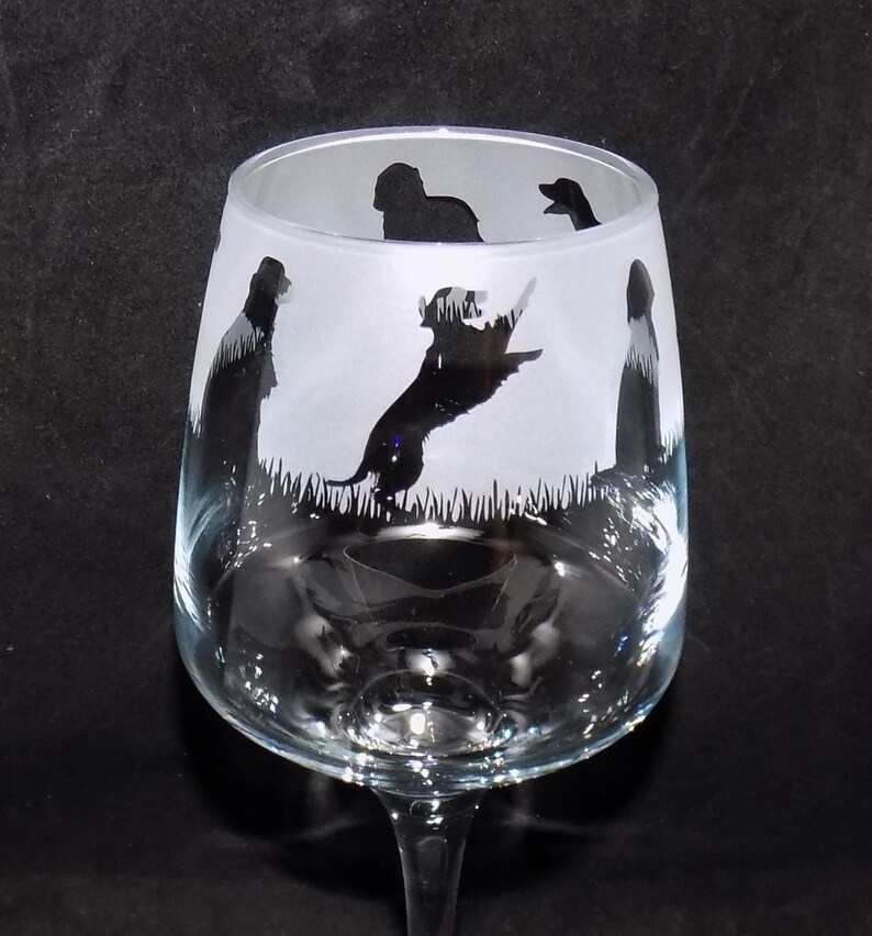 May include: A clear glass wine glass with etched silhouettes of dogs. The dogs are in various poses, including running and standing. The glass is frosted and has a stem.