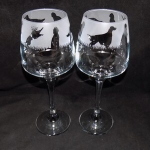 May include: Two clear glass wine glasses with etched silhouettes of dogs. The glasses have a long stem and a round bowl.