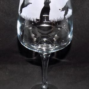 May include: A clear glass wine glass with a frosted design of four black silhouettes of dogs. The dogs are standing in a field of grass.