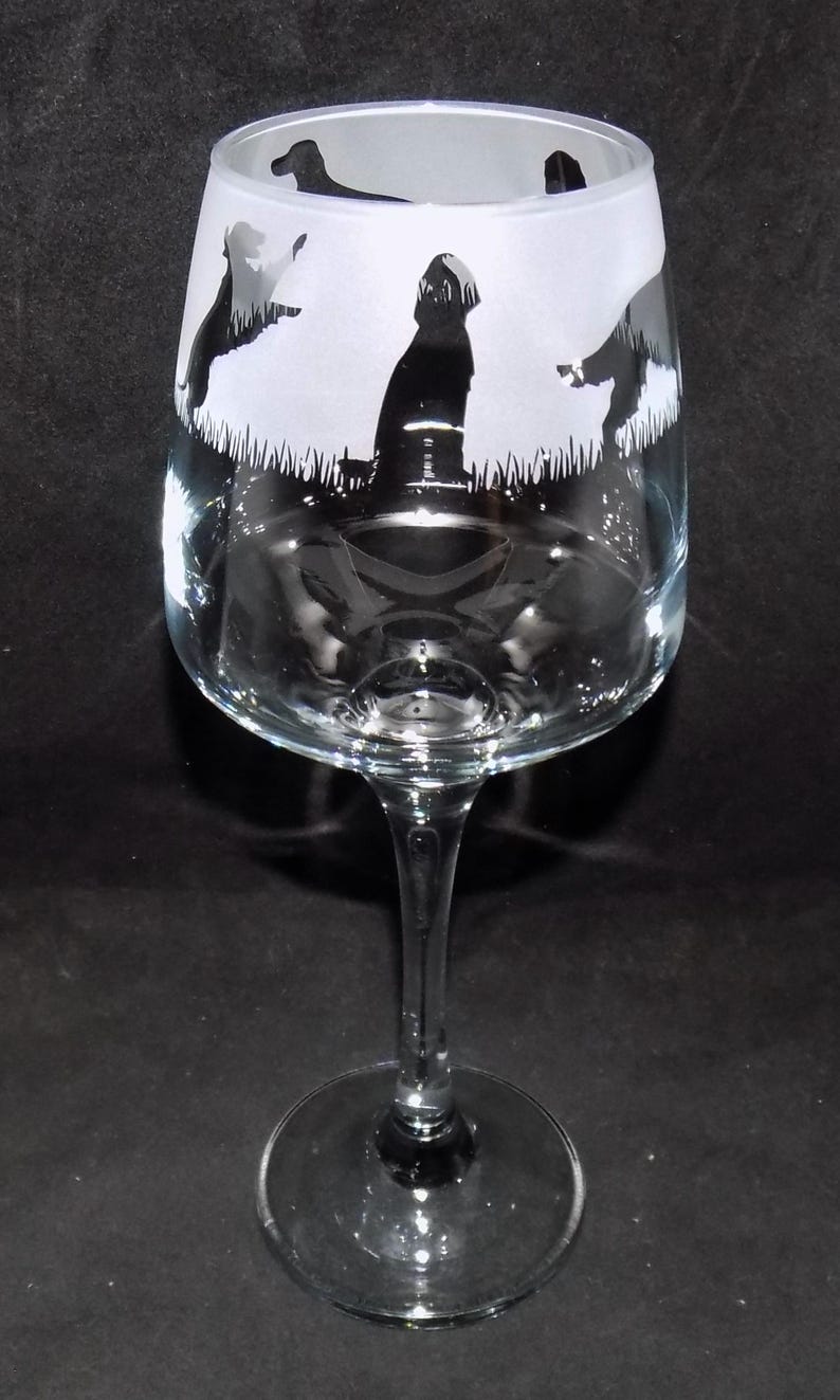May include: A clear glass wine glass with a frosted design of four black silhouettes of dogs. The dogs are standing in a field of grass.