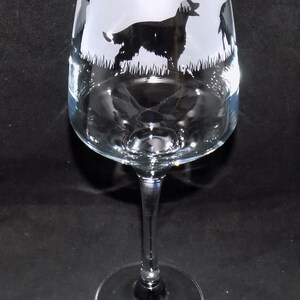 May include: A clear glass wine glass with a frosted design of black silhouettes of dogs. The dogs are in a grassy field.