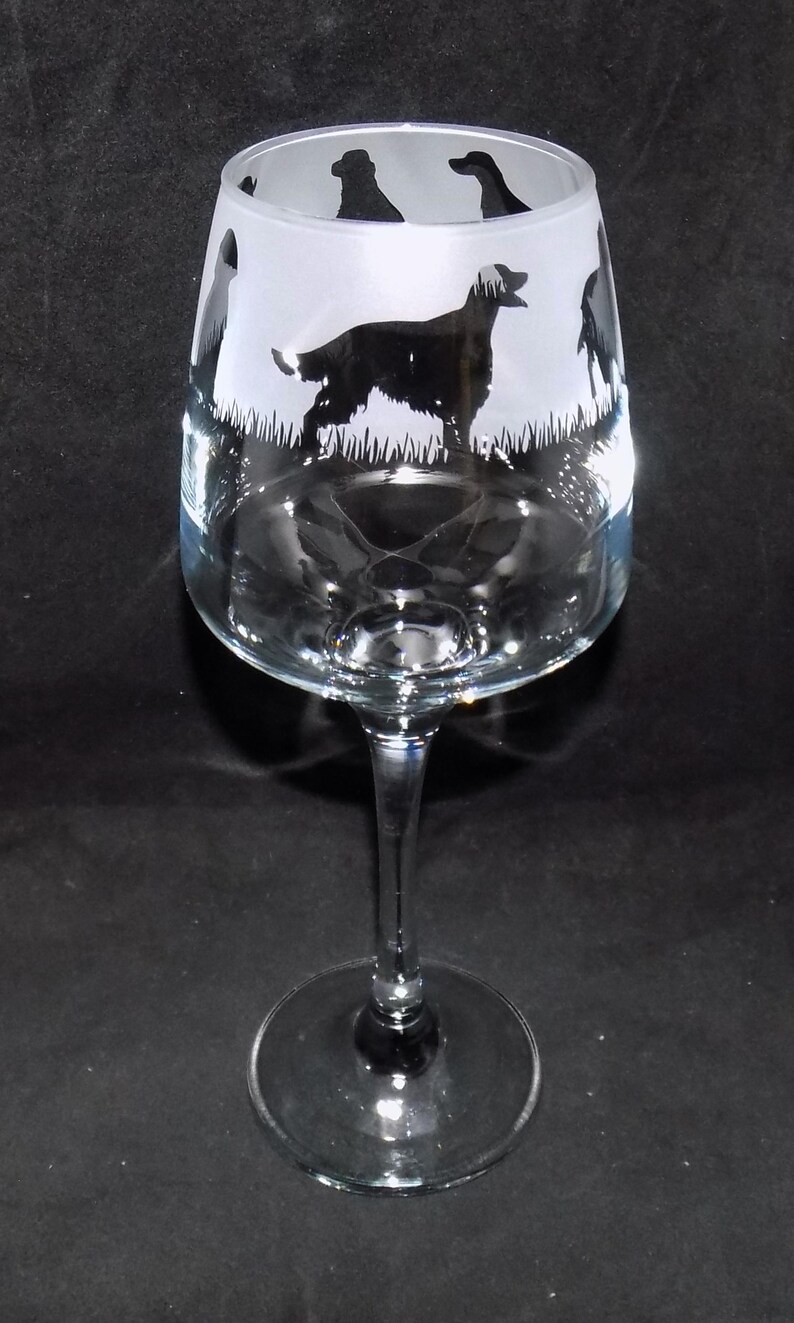 May include: A clear glass wine glass with a frosted design of black silhouettes of dogs. The dogs are in a grassy field.