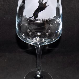 May include: A clear glass wine glass with a frosted design featuring silhouettes of dogs playing fetch. The glass has a long stem and a wide base.