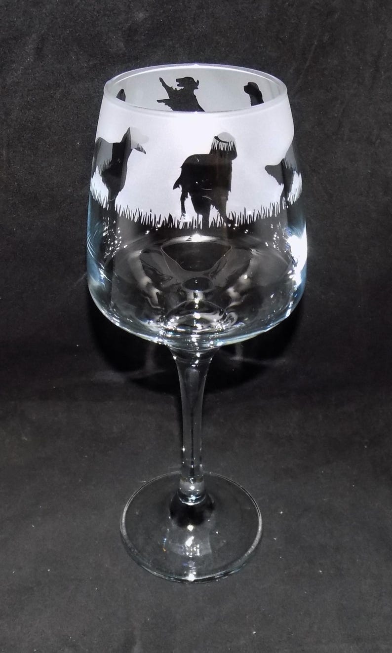 May include: A clear glass wine glass with a frosted design of four black silhouettes of dogs in a field of grass.