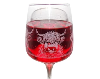 May include: A clear glass goblet filled with a deep red liquid, featuring an etched white graphic of a Highland cow with long horns and shaggy fur. The design wraps around the bowl of the glass, showcasing the detailed facial features of the animal.