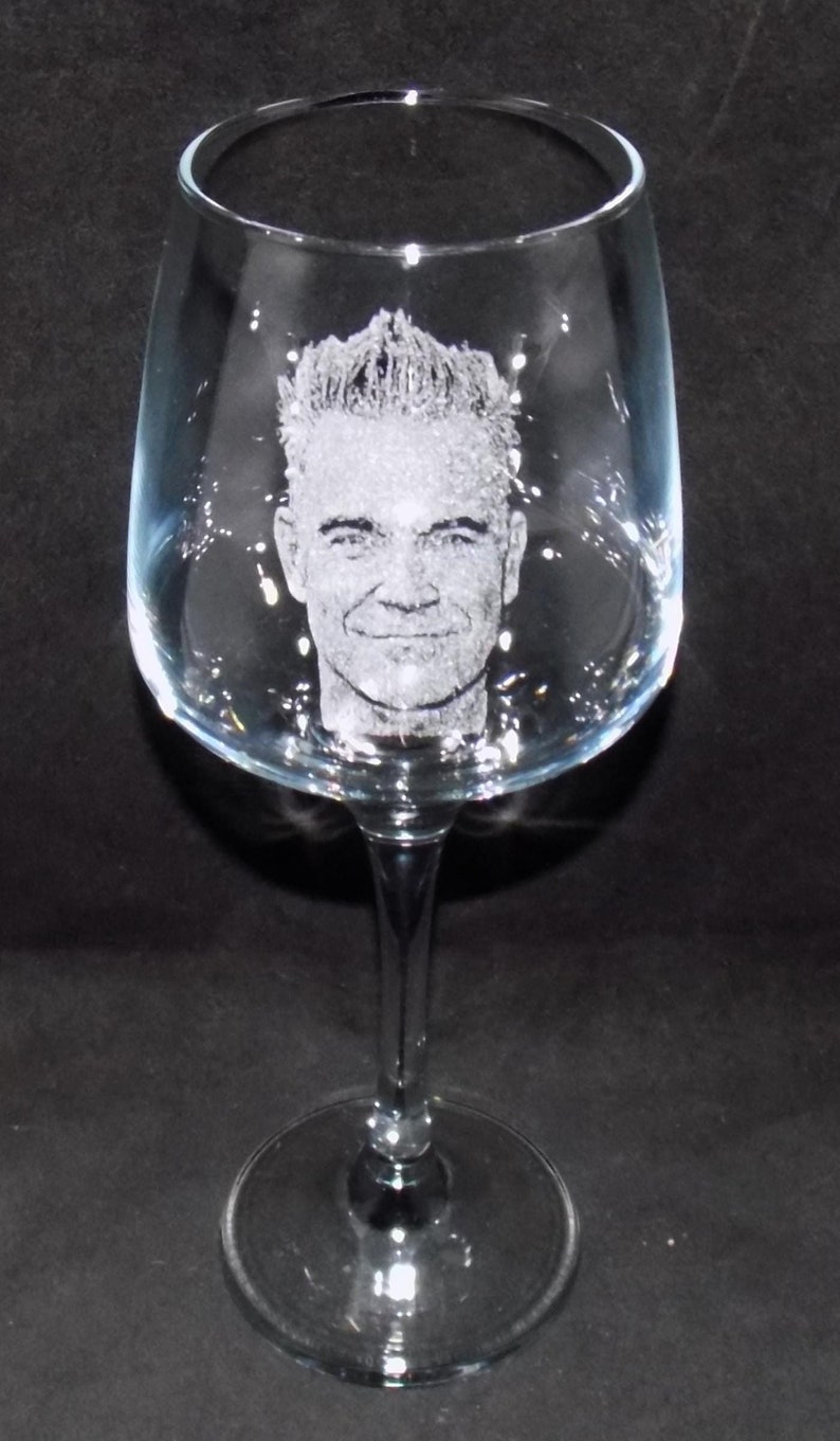 May include: A clear glass wine glass with a man's face etched into the side.