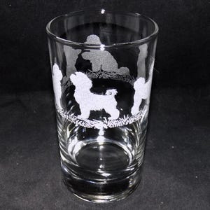 May include: A clear glass tumbler with an etched design of five white poodle silhouettes. The poodles are in various poses, some standing, some sitting, and some running.