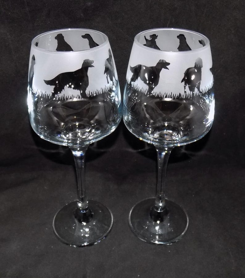 May include: Two clear glass wine glasses with etched silhouettes of dogs. The glasses have a frosted finish and are perfect for any dog lover.
