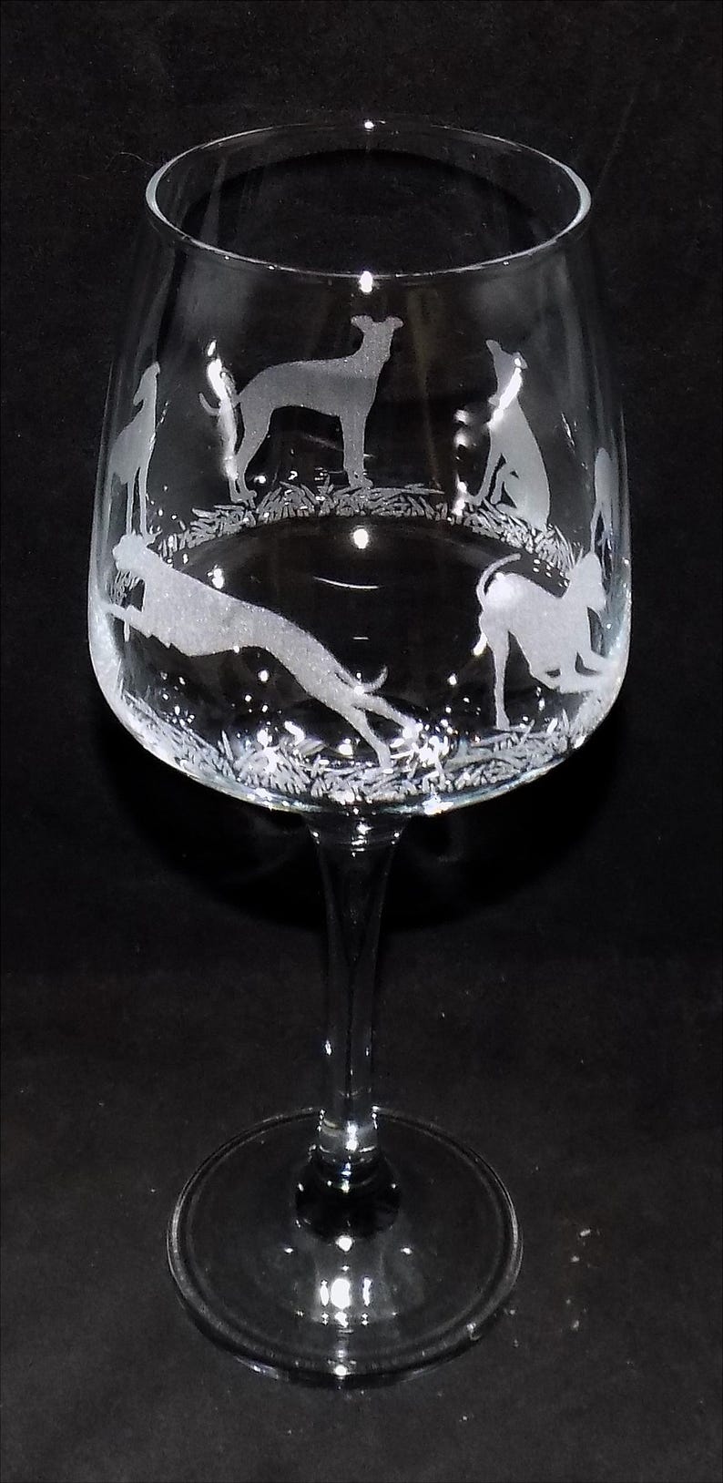 K&ouml;nnte beinhalten: Ein Weinglas aus klarem Glas mit ge&auml;tzten wei&szlig;en Silhouetten von Windhunden in verschiedenen Posen, darunter stehend, sitzend und rennend, die in einem kreisf&ouml;rmigen Muster um den Kelch &uuml;ber einem schlanken Stiel und Fu&szlig; angeordnet sind.