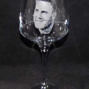 May include: A clear glass wine glass with a man's face etched into the side.