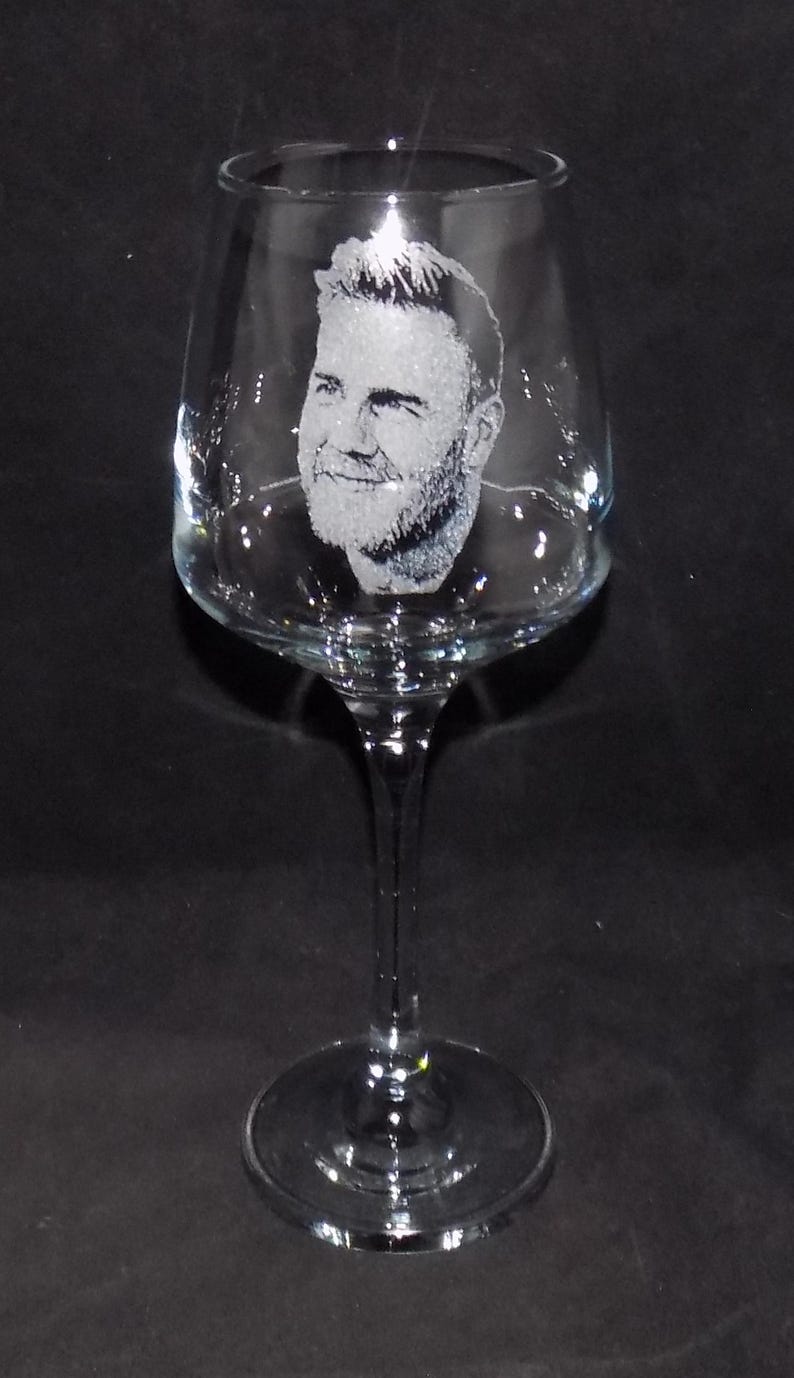May include: A clear glass wine glass with a man's face etched into the side.