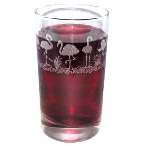 May include: A clear glass tumbler filled with a dark red liquid, featuring an etched design around the upper portion that depicts a repeating pattern of flamingos standing in grassy terrain, creating a textured white silhouette against the glass.