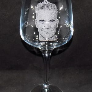 May include: A clear glass wine glass with a personalized etched image of a man's face.